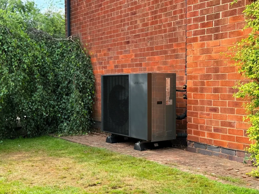 Samsung air source heat pump unit installed outside a brick house with insulated pipe connections